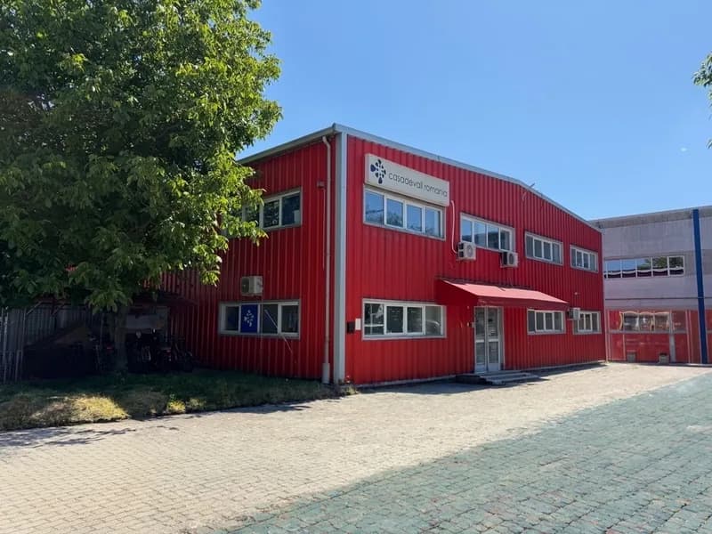 The Casadevall Romania factory, a red-clad production building behind trees.